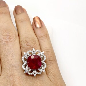 May include: A silver ring with a large, red, cushion-cut gemstone surrounded by smaller, white gemstones.