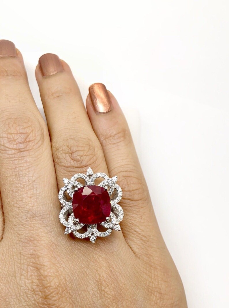 May include: A silver ring with a large, red, cushion-cut gemstone surrounded by smaller, white gemstones.