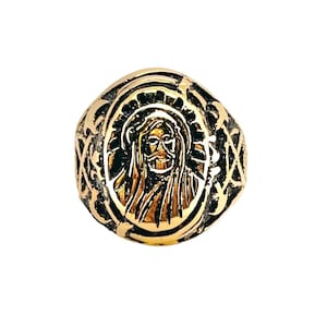 May include: A gold-toned ring with a detailed design featuring a depiction of Jesus Christ's face in the center.