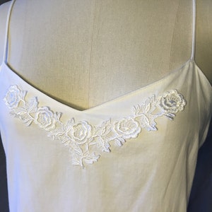 K&ouml;nnte beinhalten: Wei&szlig;es &auml;rmelloses Oberteil mit einer zarten floralen Spitzenborte am Ausschnitt.