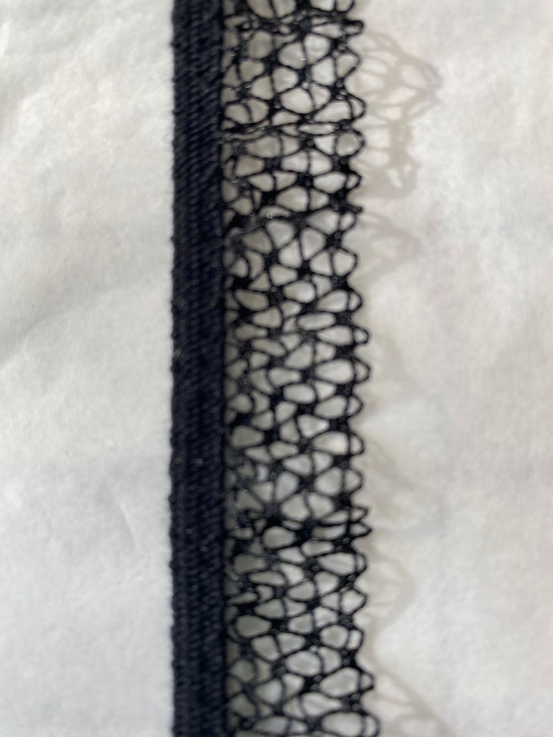 May include: Black lace trim with a delicate floral pattern. The trim is about 1 inch wide and has a soft, flexible texture.