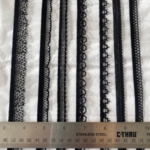 May include: Ten samples of black lace trim, each with a different pattern, are displayed on a white surface. A ruler is placed below the samples, with the numbers 3 through 10 visible.