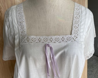 May include: White cotton nightgown with a square neckline and lace trim. The neckline is accented with a lavender ribbon.