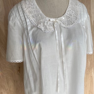 May include: White cotton nightgown with a lace collar and a satin bow. The nightgown has short sleeves and a gathered bodice.