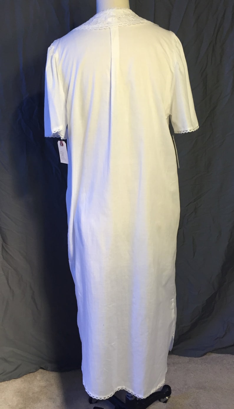 May include: White cotton nightgown with a lace trim around the neckline and sleeves. The nightgown has a button-up front and a straight silhouette.