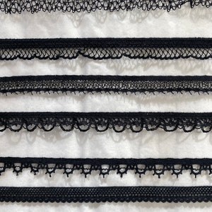 May include: Six different black lace trims with varying patterns and widths. The trims are arranged in rows on a white background.