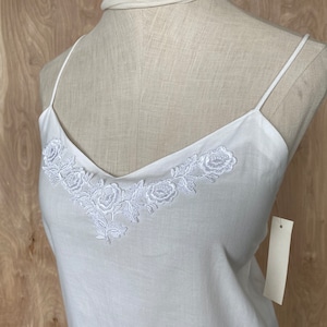 K&ouml;nnte beinhalten: Wei&szlig;es Baumwoll-Camisole-Top mit einem zarten floralen Stickmuster am Ausschnitt.