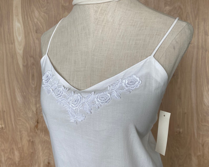 K&ouml;nnte beinhalten: Wei&szlig;es Baumwoll-Camisole-Top mit einem zarten floralen Stickmuster am Ausschnitt.