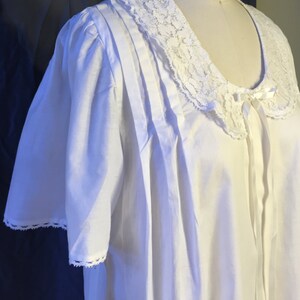 May include: White cotton nightgown with a lace collar and short sleeves. The collar has a bow at the center.