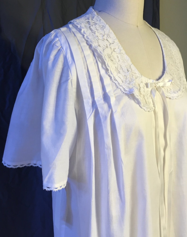 May include: White cotton nightgown with a lace collar and short sleeves. The collar has a bow at the center.