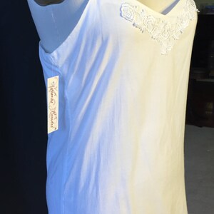 K&ouml;nnte beinhalten: Wei&szlig;es Schlupfkleid mit zarter Spitzenborte und Blumenstickerei am Ausschnitt. Das Kleid befindet sich auf einer wei&szlig;en Puppe. Das Etikett lautet "Katherine Hamnett".