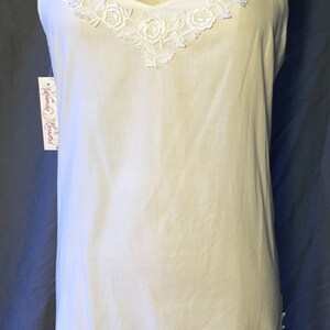 K&ouml;nnte beinhalten: Wei&szlig;es Schlupfkleid mit zarter Blumenstickerei am Ausschnitt. Das Kleid hat d&uuml;nne Tr&auml;ger und eine schlichte, flie&szlig;ende Silhouette. Das Etikett lautet "Katherine Heigl".