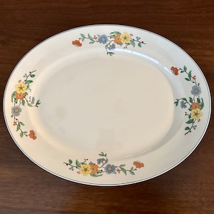May include: A white oval serving platter with a blue, yellow, and orange floral design around the rim.