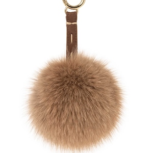 Puede incluir: Un llavero de pompón de piel sintética marrón con una correa de cuero marrón y un anillo de metal dorado.