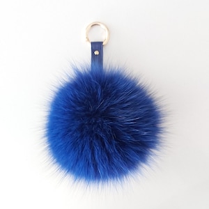 May include: A blue faux fur pom pom keychain with a gold metal ring and a blue leather strap.