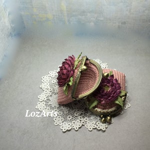 May include: Two pink crocheted coin purses with floral embellishments and gold metal clasps. The purses are on a white doily.