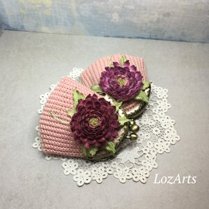 May include: Two pink crocheted coin purses with floral embellishments. The purses have a vintage-style clasp and are sitting on a white lace doily.