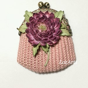 May include: A pink crocheted coin purse with a pink and green fabric flower and a brass clasp. The purse has the text "LozArts" on the bottom.