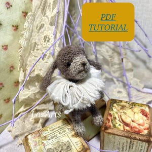 May include: A crocheted gray bunny with a white ruffle collar sits on top of two wooden blocks. The blocks have vintage-style designs and text. The text on one block reads "Golden West Post". The text on the other block reads "Banking Co.". A yellow sign above the bunny reads "PDF TUTORIAL".