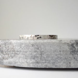 May include: A silver hammered band ring. The ring is smooth and has a textured surface.