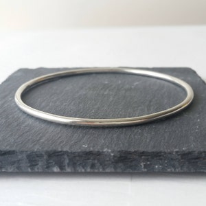 May include: A simple silver bangle bracelet. The bracelet is smooth and round, with a polished finish.