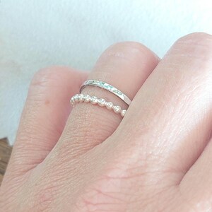 May include: Two silver rings on a finger. The top ring is a simple band, while the bottom ring is a beaded ring.