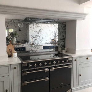 May include: A black range with a stainless steel trim and multiple knobs. The range is in a kitchen with white cabinets and a mirrored backsplash.