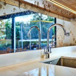 May include: A modern kitchen sink with a chrome faucet and a white worktop. The sink is made of stainless steel and has a single bowl. The faucet has a high arc spout and a lever handle. The worktop is made of quartz and has a smooth, polished finish.