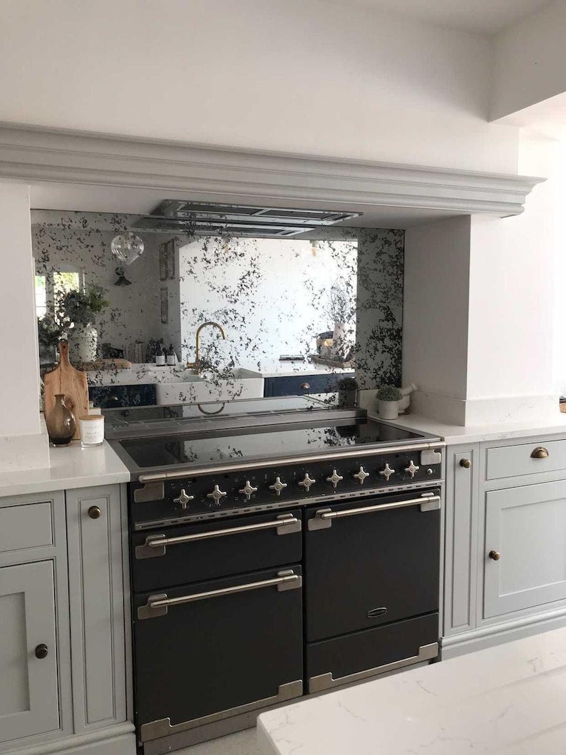 May include: A black range with a stainless steel trim and multiple knobs. The range is in a kitchen with white cabinets and a mirrored backsplash.
