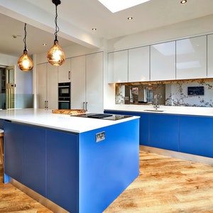 May include: A modern kitchen with white cabinets and blue island cabinets. The island has a white countertop and a built-in hob. The backsplash is a mirrored tile with a distressed finish.