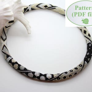 Puede incluir: Un collar de cuentas negras, blancas y plateadas con un patrón geométrico. El collar está sobre una superficie blanca. Patrón (archivo PDF)