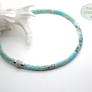 May include: A turquoise, blue, and gold beaded necklace with a silver magnetic clasp. The necklace is made with seed beads and has a geometric pattern.