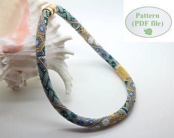 Puede incluir: Un collar de cuentas con un patrón azul, blanco y dorado. El collar está hecho de cuentas pequeñas y tiene un cierre de broche. El collar se muestra sobre una concha blanca.