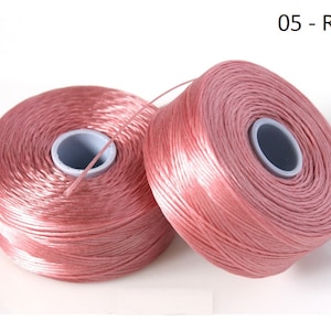 Pode incluir: Dois carret&eacute;is de fio cor de rosa. O fio est&aacute; enrolado em torno de um carretel de pl&aacute;stico branco com um centro preto. Os carret&eacute;is est&atilde;o sobre um fundo branco. 05 - Rose