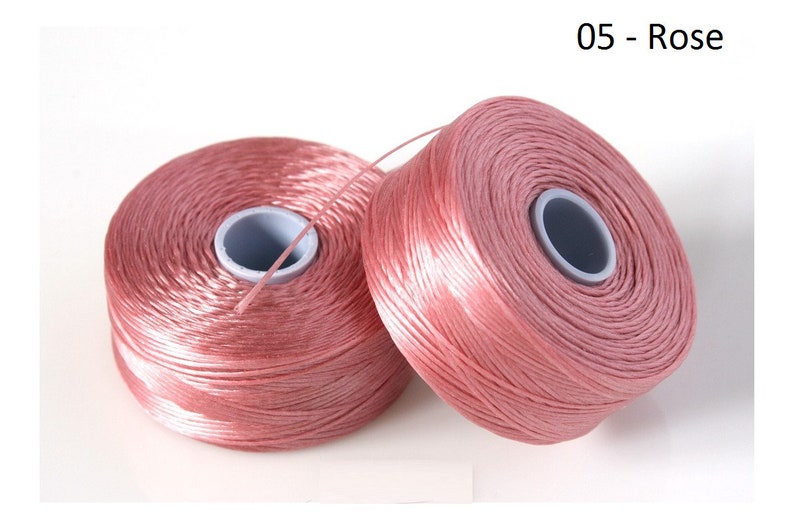 Pode incluir: Dois carret&eacute;is de fio cor de rosa. O fio est&aacute; enrolado em torno de um carretel de pl&aacute;stico branco com um centro preto. Os carret&eacute;is est&atilde;o sobre um fundo branco. 05 - Rose