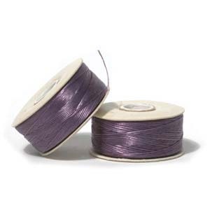 May include: Two spools of purple cord, one leaning against the other. The spools are made of cardboard with the cord wrapped around them. The cord has a shiny, metallic appearance. The spools are on a white background.