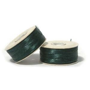 May include: Two spools of dark green thread. The thread is wound around a light-colored cardboard core. One spool is tilted, and the other is upright. The background is white.