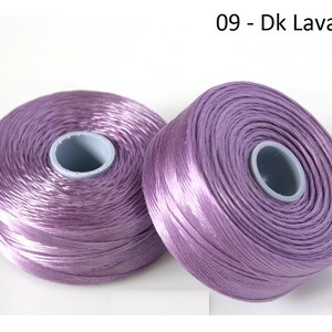 Pode incluir: Dois carret&eacute;is de fio de cor lavanda. Os carret&eacute;is s&atilde;o de pl&aacute;stico e t&ecirc;m um r&oacute;tulo branco com o texto "09 - Dk Lavander".
