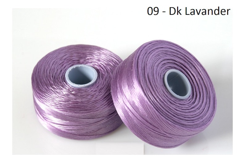 Pode incluir: Dois carret&eacute;is de fio de cor lavanda. Os carret&eacute;is s&atilde;o de pl&aacute;stico e t&ecirc;m um r&oacute;tulo branco com o texto "09 - Dk Lavander".