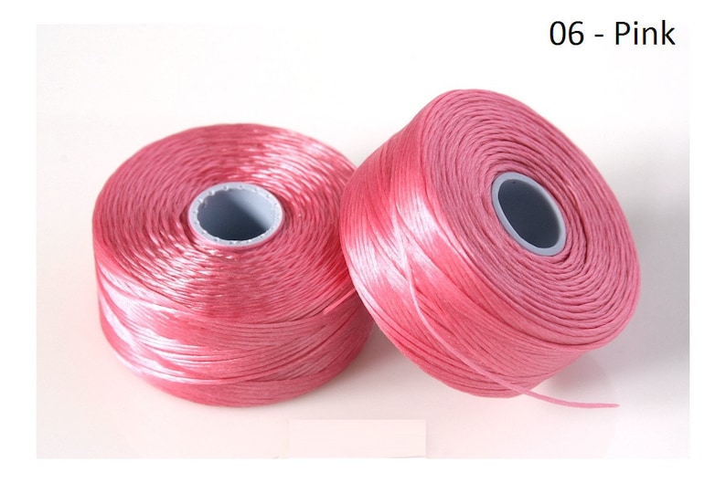Pode incluir: Dois carret&eacute;is de fio rosa, cada um enrolado em torno de uma bobina de pl&aacute;stico branca. Os carret&eacute;is s&atilde;o etiquetados com "06 - Rosa".