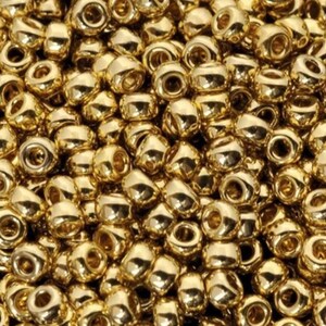Puede incluir: Primer plano de un montón de pequeñas cuentas brillantes de color dorado. Las cuentas son redondas con un agujero en el centro y reflejan la luz, creando un efecto brillante. Las cuentas están densamente empaquetadas.