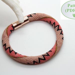 Può includere: Un braccialetto di perline rosa e nero con una chiusura in oro rosa. Il braccialetto ha un motivo a zig-zag. Modello (file PDF)