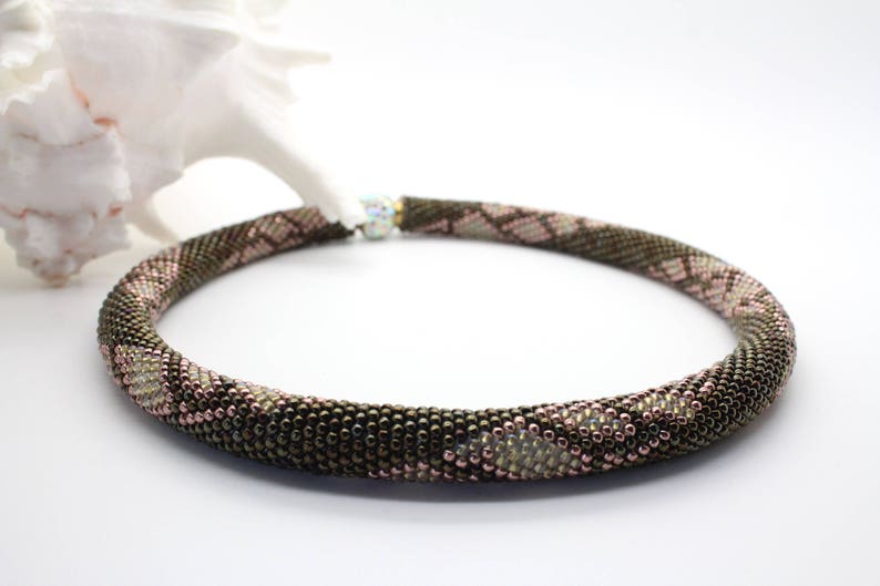 May include: A brown and pink beaded necklace with a snake skin pattern.