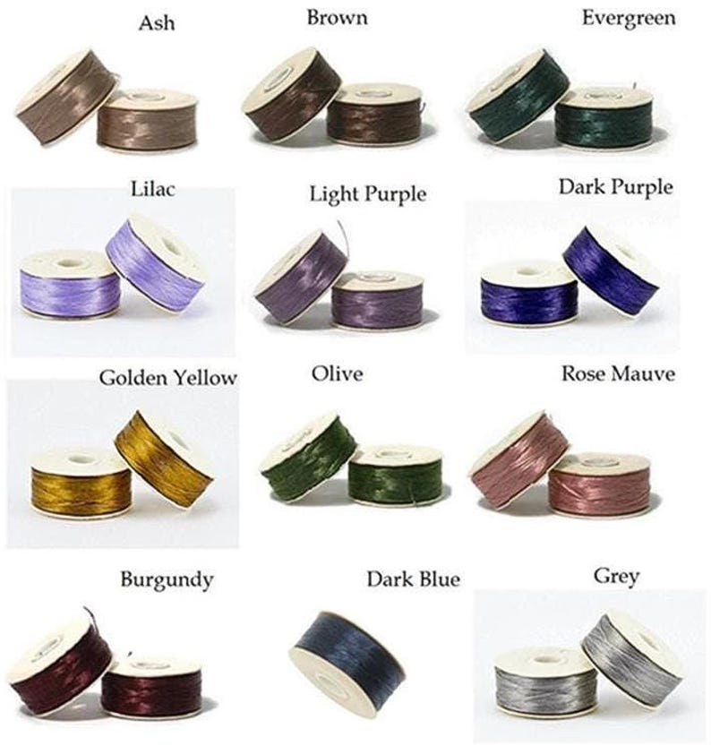 May include: A collection of spools of thread in various colors, including ash, brown, evergreen, lilac, light purple, dark purple, golden yellow, olive, rose mauve, burgundy, dark blue, and grey. Each spool is labeled with its color.