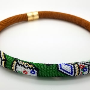 May include: A green, brown, white, blue, and gold beaded necklace with a playing card design. The necklace is made of seed beads and is approximately 18 inches long.