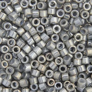 Könnte beinhalten: Nahaufnahme eines Haufens kleiner, zylindrischer, silberner Perlen. Die Perlen sind gleichmäßig groß und geformt, mit einem metallischen Glanz. Sie sind zufällig verstreut und bilden eine strukturierte Oberfläche. Ideal für Schmuckherstellung und Bastelprojekte.