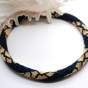May include: A dark blue beaded necklace with gold accents, resembling a snake skin pattern.