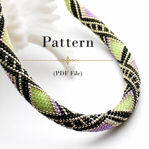 Könnte beinhalten: Eine röhrenförmige Perlenkette mit einem geometrischen Muster aus schwarzen, lindgrünen und lavendelfarbenen Saatperlen. Der Text Pattern (PDF File) ist in der Mitte der geschwungenen Kette platziert, die vor einem schlichten weißen Hintergrund liegt.