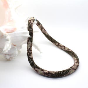 May include: A brown and pink beaded necklace with a geometric pattern. The necklace is made of small beads and is approximately 46 cm long.