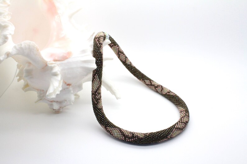 May include: A brown and pink beaded necklace with a geometric pattern. The necklace is made of small beads and is approximately 46 cm long.